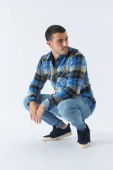 Sobrecamisa de algodón para hombre con interior de corderito, estampado a cuadros en tonos negro, blanco y azul. Tiene cierre de botones, bolsillos tipo cartera y logo en goma. El modelo usa talle M.