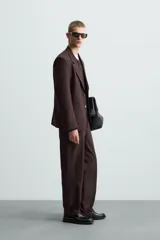 Pantalón de vestir color marrón oscuro, de corte recto, con bolsillos laterales y traseros de doble vivo. Se ajusta a la cintura con cierre de cremallera y botón.