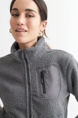 Campera negra de corderito con cierre frontal y cuello alto. Tiene un bolsillo con cierre en el pecho y bolsillos laterales.