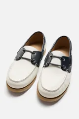 Zapato náutico de cuero blanco con detalles en negro y suela marrón.
