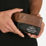 Pack compuesto por una remera negra de manga corta con estampado del logo de la marca en el pecho y una billetera marrón de cuero sintético con compartimentos interiores para tarjetas y billetes.