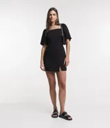 Vestido corto negro de viscosa con escote cuadrado, mangas cortas abullonadas, lastex en la espalda y abertura en el bajo.