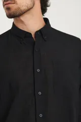 Camisa azul marino de lino y algodón, con cuello abotonado, manga larga con puños enrollados, bolsillo de parche en el pecho y cierre frontal con botones.
