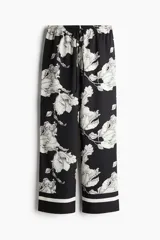 Pantalón de sarga suave con estampado floral en blanco y negro, tiro alto, cintura elástica con cordón ajustable, piernas rectas con puño en el bajo y detalle de doble línea blanca en el ruedo.