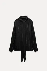 Blusa negra con cuello redondo con lazo en el mismo tejido, manga larga con puño y detalle de hilo metalizado.