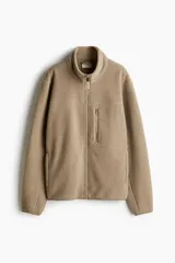 Campera deportiva color beige en tejido sherpa, con cuello alto, cierre frontal, bolsillo superior con cierre, bolsillos laterales con cierre, puños y bajo con elástico fino.