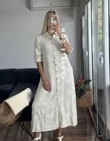 Vestido camisero midi color crudo con bordado floral, cuello camisero, mangas 3/4 con trabilla y abertura lateral. Incluye cinturón de soga con hebilla de madera.