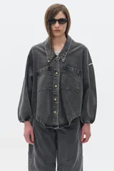 Camisa de jean oversized, color gris oscuro, con escote en V bajo, cuello camisero y mangas abullonadas. Tiene bolsillos delanteros y cierre con botones metálicos.