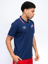 Remera polo azul con cierre, puños y cuello con detalle tricolor. Incluye logo de Umbro y escudo del Club Nacional de Football.