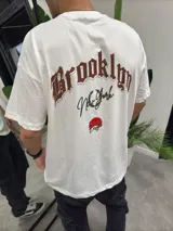 Remera blanca de corte oversize con estampa en la espalda que dice "Brooklyn New York" en color marrón y un círculo rojo debajo.