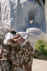 Camisa de manga larga con puños elásticos, color blanco con rayas verticales finas color beige. Tiene cuello camisero, cierre frontal con botones y un bolsillo de parche en el pecho.