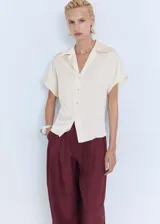 Camisa color crema de manga corta con tejido satinado, corte regular, cuello camisero y cierre delantero con botones.