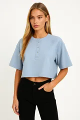 Remera cropped color rosa con cuello redondo, manga 3/4 y cierre frontal con broches.