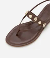 Sandalia marrón de cuero sintético, con tiras finas, apliques de conchas doradas y cierre con hebilla.