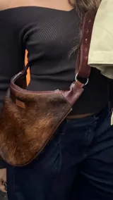 Cartera bandolera de cuero con pelo animal print marrón y blanco, correa de cuero ajustable con hebilla y cierre con cremallera.