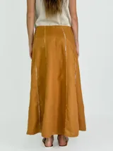 Pollera larga negra de corte amplio, con costuras verticales que simulan pliegues y terminaciones deshilachadas. Se combina con una musculosa negra de escote redondeado.