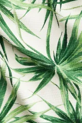 Traje de baño enterizo strapless con estampado de hojas de palmera en tonos de verde sobre fondo blanco. Tiene detalle metálico en el centro del busto, copas con relleno extraíble, reborde de silicona en la parte superior y corte alto en las piernas.