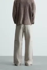 Pantalón de algodón color beige claro, estilo relaxed fit, con cintura ajustable mediante cinturón de tela a juego. Presenta cinco bolsillos, bolsillos laterales de vivo y costuras laterales giradas hacia adelante.