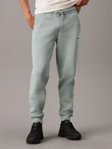 Pantalón de chándal de felpa color verde agua, con cintura elástica ajustable con cordón, puños de canalé, bolsillos laterales y trasero, y logo bordado de Calvin Klein en la pierna.