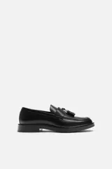 Mocasín de vestir de cuero negro, con puntera redondeada y detalle de borlas en la parte delantera.