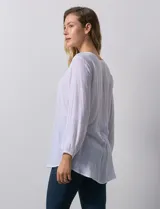 Blusa blanca de manga larga con cuello a la base y escote en V con botones. Terminación de manga con elástico.