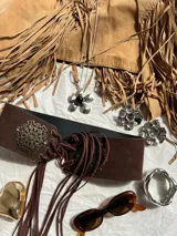 Faja ancha de cuero sintético color marrón con detalles metálicos dorados de estilo boho y cordones de ajuste con flecos.