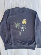 Buzo negro de corte oversize con cuello redondo y puños acanalados. Estampado en la espalda con dos palmeras y un sol en tonos verde y amarillo.