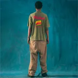 Remera verde militar de corte oversize con cuello redondo y estampado frontal con la frase "Caldo de Barrio" en letras rojas.