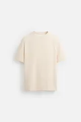 Camiseta color crema de corte relaxed fit, confeccionada en tejido de algodón compacto con estructura piqué. Tiene cuello redondo y mangas cortas.