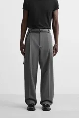 Pantalón gris de corte ancho con pliegues frontales y cinturón fino negro.