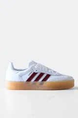Zapatillas Adidas Samba de cuero blanco con puntera de gamuza gris y tres tiras de cuero bordó. Suela de goma color caramelo traslúcida.