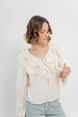 Blusa color crema con volados en el frente, detalle de puntilla y bordados florales en mangas.