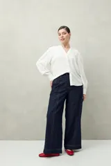 Camisa celeste de manga larga con cuello redondo y escote en V. Presenta detalles de pasamanería en el frente y las mangas, y botones forrados al tono. De corte fluido.