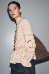 Camisa color crema de algodón con cuello alto, manga larga con puños con volantes y bordados a tono.