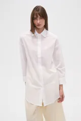 Camisa blanca de algodón con cuello clásico, corte holgado, cierre frontal con botones y mangas largas.