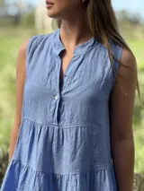 Vestido verde militar de lino, corte a la rodilla, sin mangas, con cuello mao y botones de nácar. Presenta varios cortes en su largo, aportando movimiento y un toque moderno a este diseño fresco y elegante.