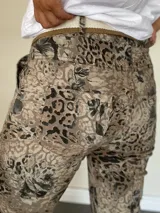 Pantalón de mujer con estampado animal print y detalles florales en tonos beige y negro, de corte recto y con ruedo doblado. Incluye un cinturón de tela beige y marrón.