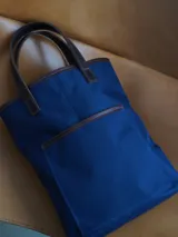 Bolso matero de lona color azul con detalles en cuero marrón, con asas cortas y logo de la marca en cuero.
