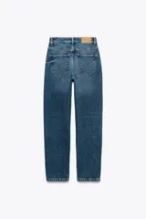 Pantalón de jean gris oscuro, de corte mom fit, tiro alto y largo tobillero. Cuenta con cinco bolsillos, cierre frontal con cremallera y botón.