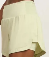 Bermuda deportiva femenina de microfibra color amarillo claro, con diseño de doble capa: un short interno ajustado y una capa externa suelta con bajo redondeado. Posee cintura alta.
