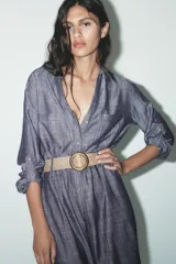 Vestido camisero azul con cinturón de rafia, de cuello solapa y manga tres cuartos con trabilla y botón. Tiene bolsillos de parche en el delantero y cierre frontal con botones.