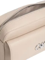 Cartera cruzada rectangular de piel sintética color beige claro, con solapa frontal y cierre de cremallera superior. Presenta un monograma metálico grande con las iniciales CK en tono plateado sobre la solapa. Incluye correa ajustable de cuero sintético y cadena metálica plateada.