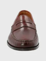 Zapato mocasín de cuero color marrón, con detalle de antifaz y suela de cuero y goma.