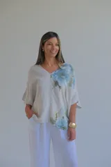Blusa beige de lino italiano con estampado floral en tonos celeste y verde en un lateral, escote en V en frente y espalda, y mangas murciélago.
