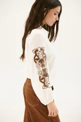 Camisa blanca de manga larga con bordados florales marrones en las mangas.