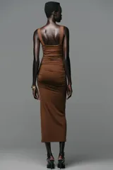 Vestido midi marrón entallado, con escote recto, tirantes y detalle de caracola metálica en los tirantes.