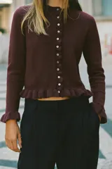 Cárdigan gris jaspeado de punto con cuello redondo y manga larga. Presenta volantes en el borde de los botones, en el bajo y en los puños.