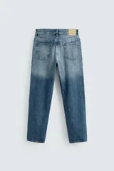 Jeans de denim de algodón, color negro lavado, con tiro medio, corte ajustado en cadera y muslos, y pierna que se estrecha hacia el tobillo. Presenta cinco bolsillos y cierre frontal con cremallera y botón.