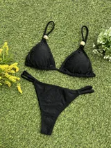 Bikini negra con corpiño triangular que tiene un aplique de piedra en el bretel y bombacha colaless con tiras ajustables laterales.