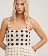 Vestido midi de algodón, color crema, con breteles finos. El corpiño presenta un diseño de crochet con motivos florales en azul marino, y la falda evasé tiene un estampado de pequeños íconos abstractos en azul.